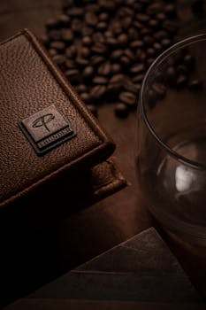 Close-up of a luxury leather wallet beside a glass and coffee beans.