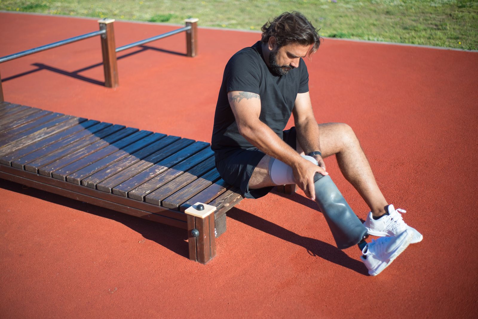 Runner outdoors adjusting a knee brace before walking on a bright path