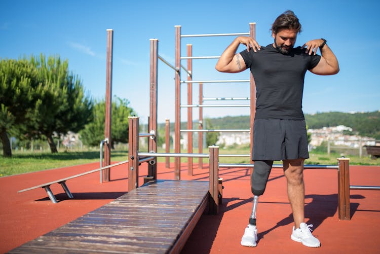 A Man Touching His Shoulders While Standing Near The Wooden Platform