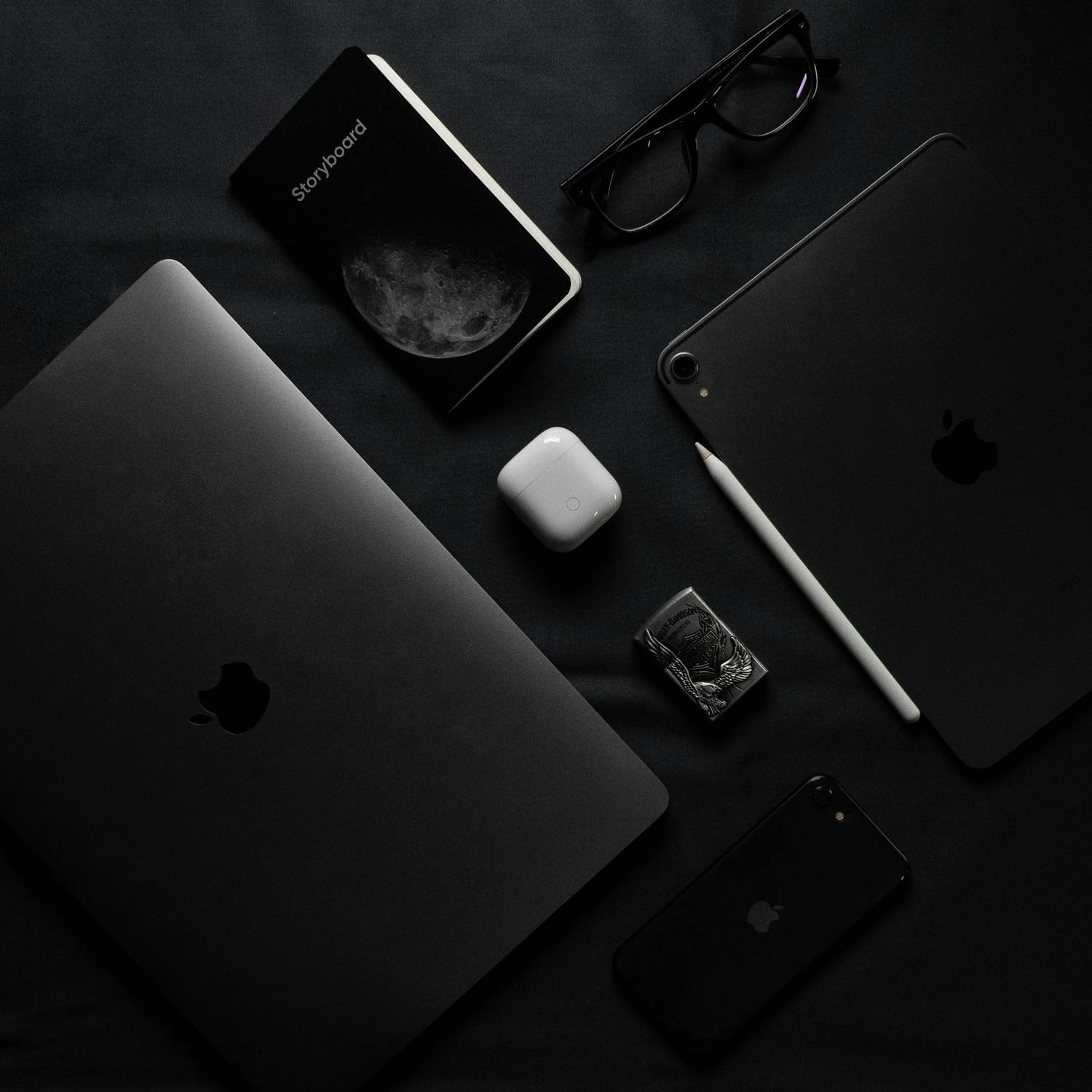 A dark minimalist flatlay of modern gadgets including laptop, smartphone, and eyeglasses.