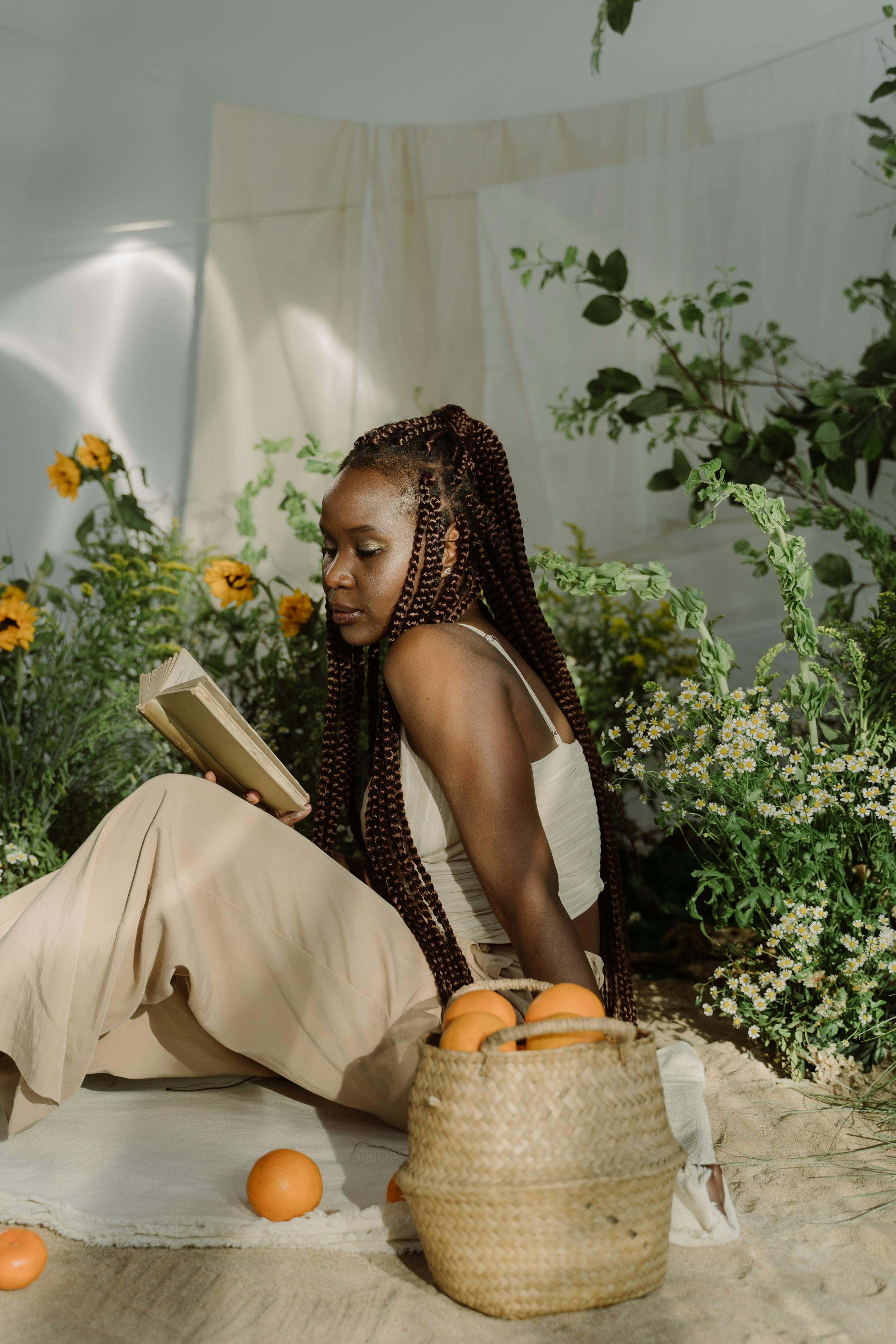 Woman with afro braids enjoying a peaceful reading time in a lush garden setting.