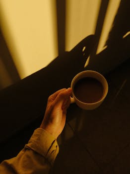 A hand holding a coffee cup against a moody background with captivating shadows.