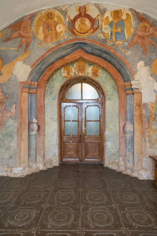 Free Wooden door set in a vibrant, historic painted archway, showcasing religious fresco art. Stock Photo