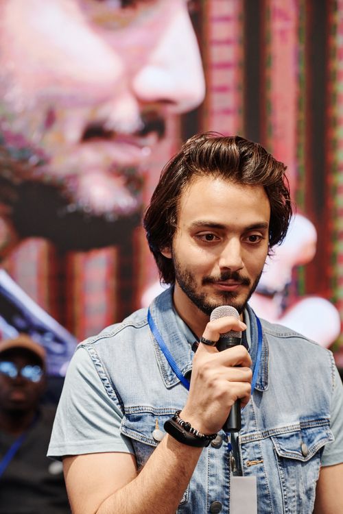 Free A young man in a denim vest giving a speech at a conference with a microphone. Stock Photo