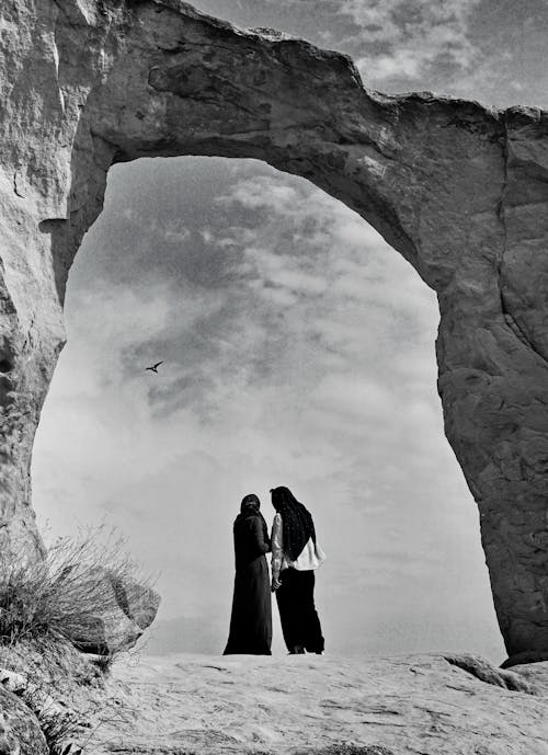 Backview of Couple standing under Arched Rock Formation 