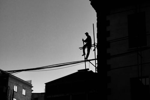 Free Dramatic silhouette of a man working on a scaffold against the city skyline at dusk. Stock Photo