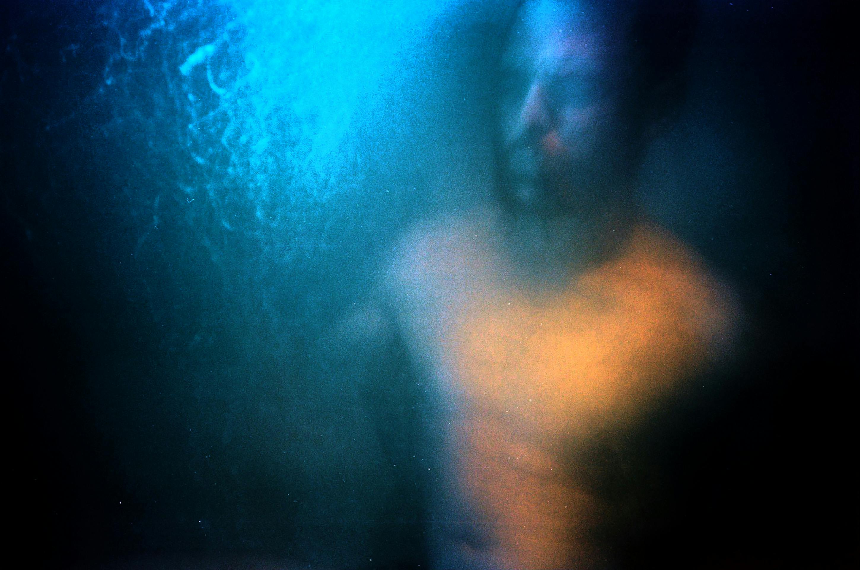 Blurred abstract portrait of a shirtless man behind frosted glass with blue and orange lighting.