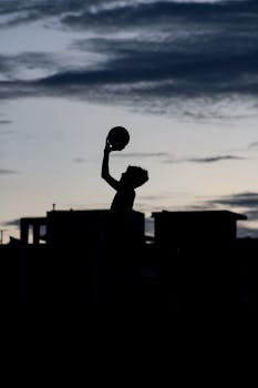 Silhouette of a person shooting a basketball against a twilight sky in Visakhapatnam, India.