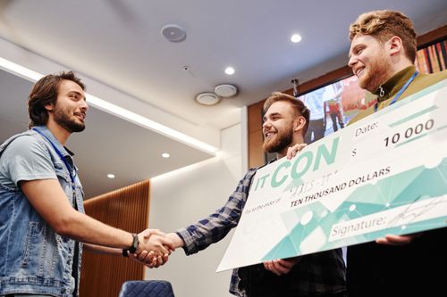 Free Two men celebrating with a $10,000 check at an indoor event, shaking hands and smiling. Stock Photo