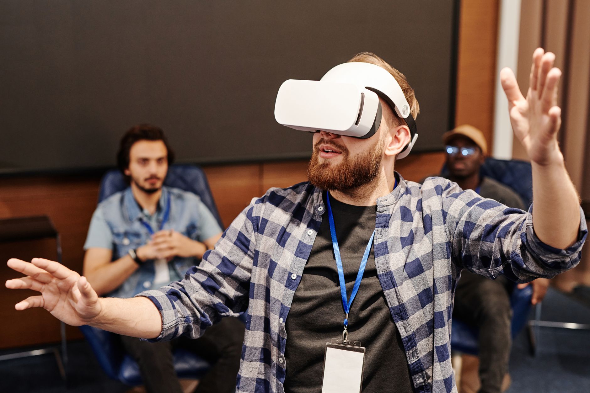 Adult man using VR headset indoors with two people in the background, exploring technology.