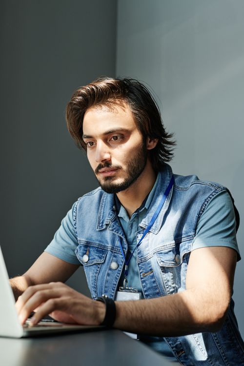 Free Focused young man with beard typing on a laptop in a bright room, highlighting productivity and concentration. Stock Photo