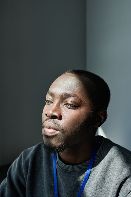 Free A thoughtful African American man gazes into the distance, illuminated by soft natural light indoors. Stock Photo
