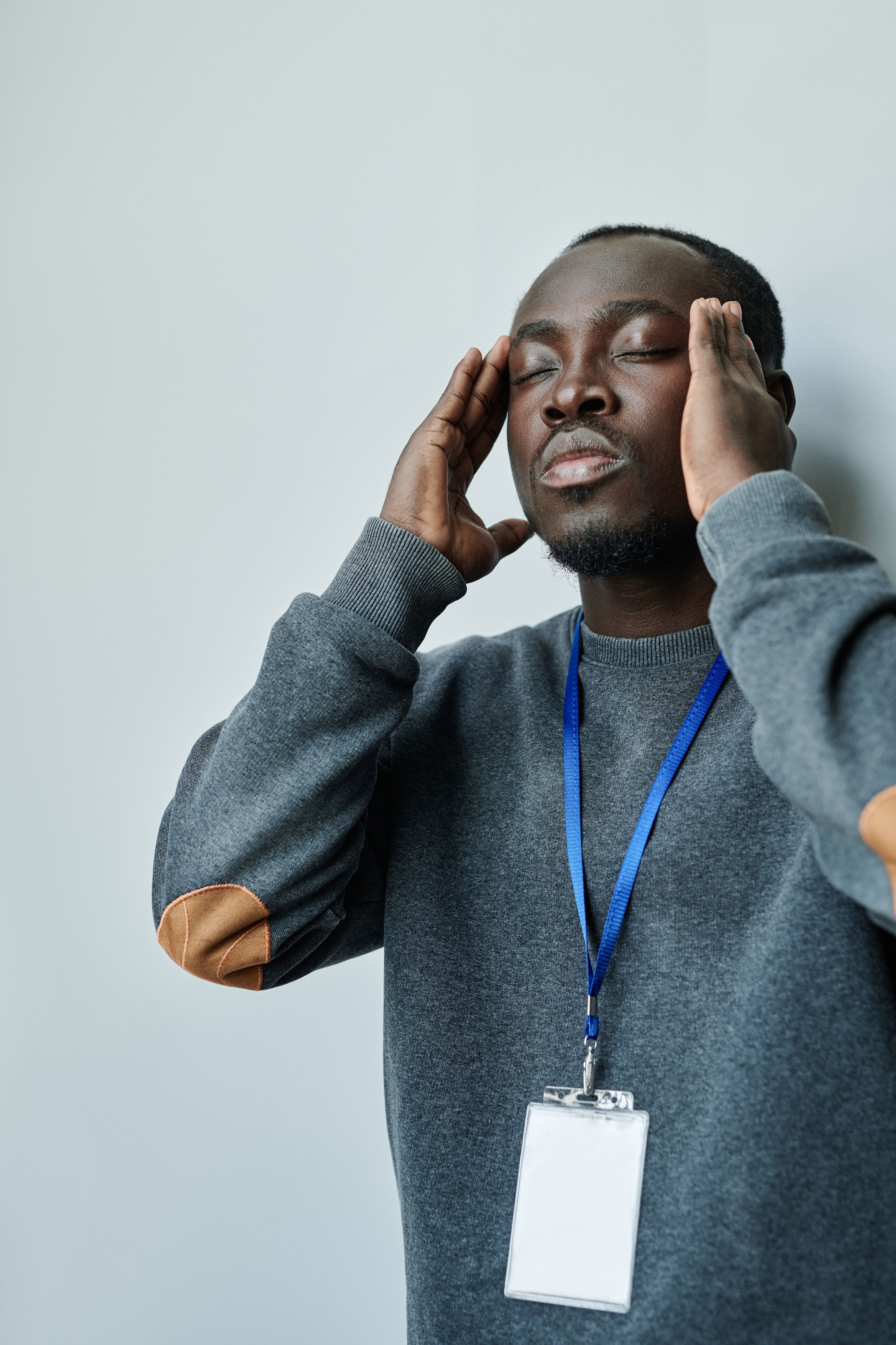 A young man in a sweater holds his head, expressing stress and exhaustion.
