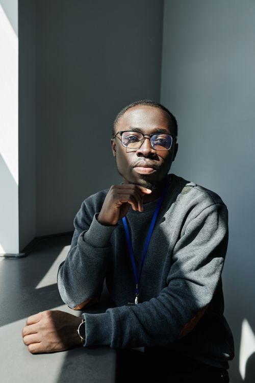 Free A man in eyeglasses and a gray sweater seated indoors, looking thoughtful. Stock Photo