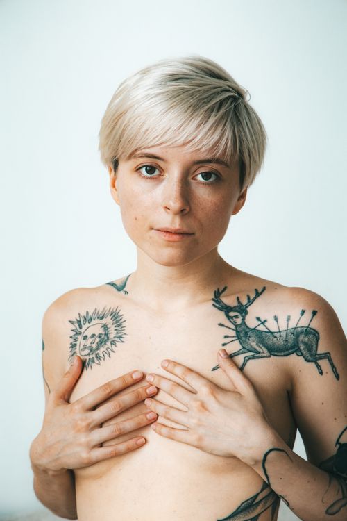 Free Minimalist portrait of a tattooed person with short hair posing in studio setting. Stock Photo