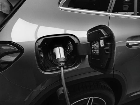 Close-up black and white image of an electric vehicle charging at a station.