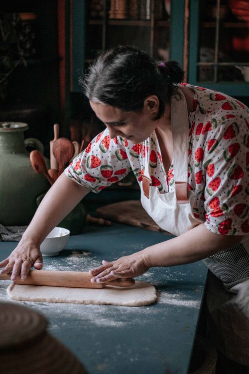 Free An adult woman in a strawberry-patterned shirt kneading dough in a rustic kitchen. Stock Photo