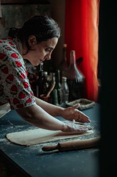 Woman kneading dough on a dark countertop with scattered flour, evoking a rustic kitchen atmosphere.