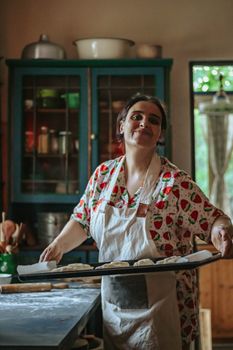 A cheerful woman in a rustic kitchen holding a baking tray of cookies, creating a warm, homey atmosphere.