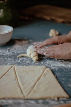 Hands rolling dough in a cozy kitchen setting, creating artisanal pastries.