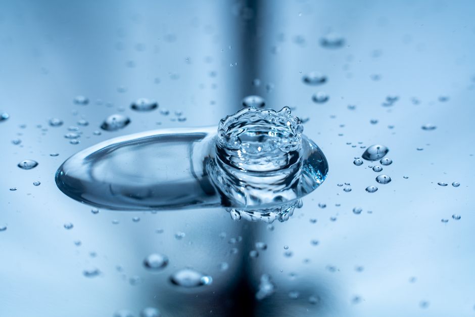 Macro shot capturing a water droplet splash creating ripples on a reflective surface.