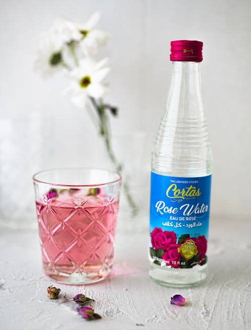 A Glass Bottle Near the Drinking Glass with Pink Liquid on a White Surface