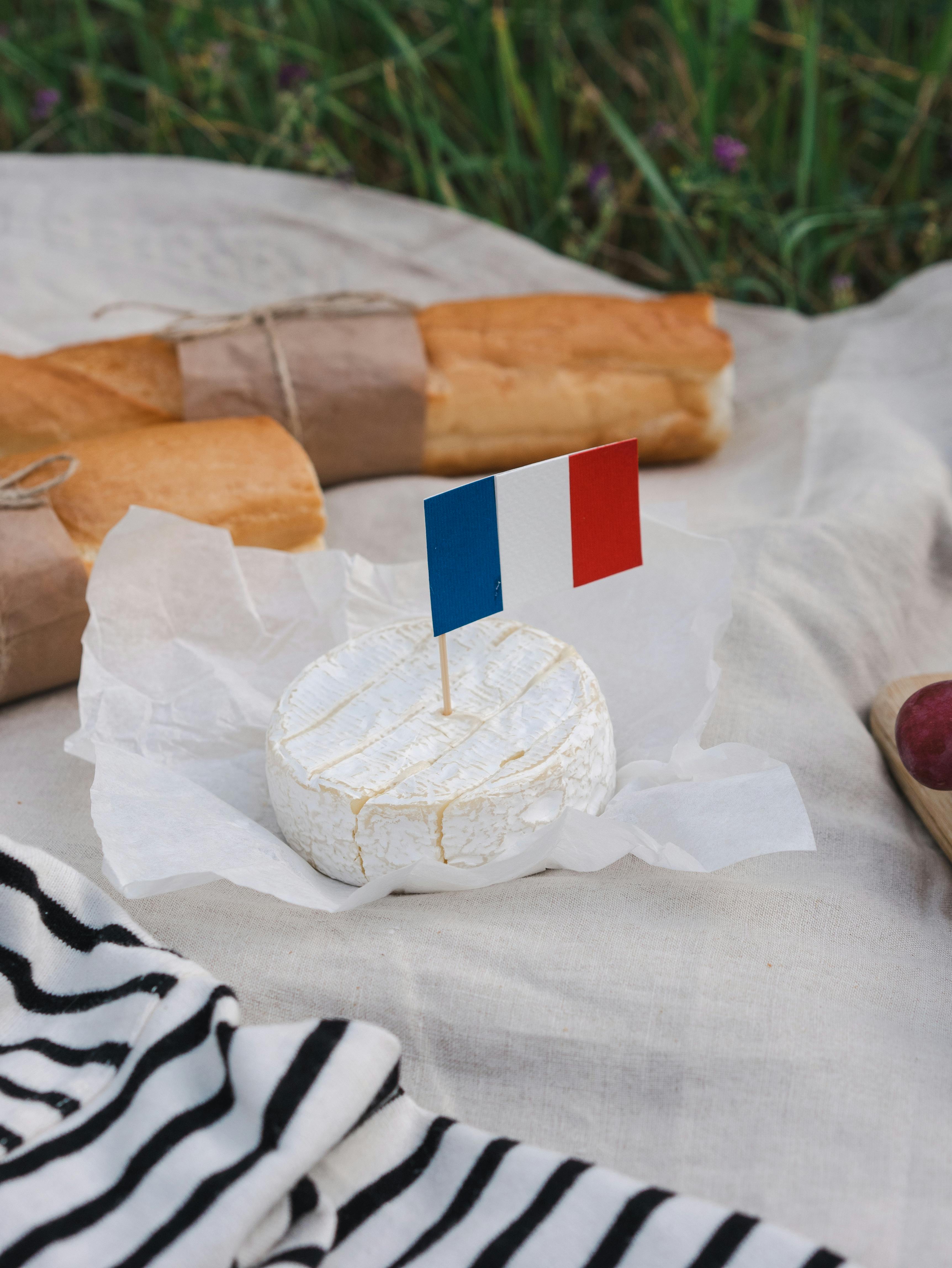 French picnic setup with camembert and baguettes on a cloth with French flag.