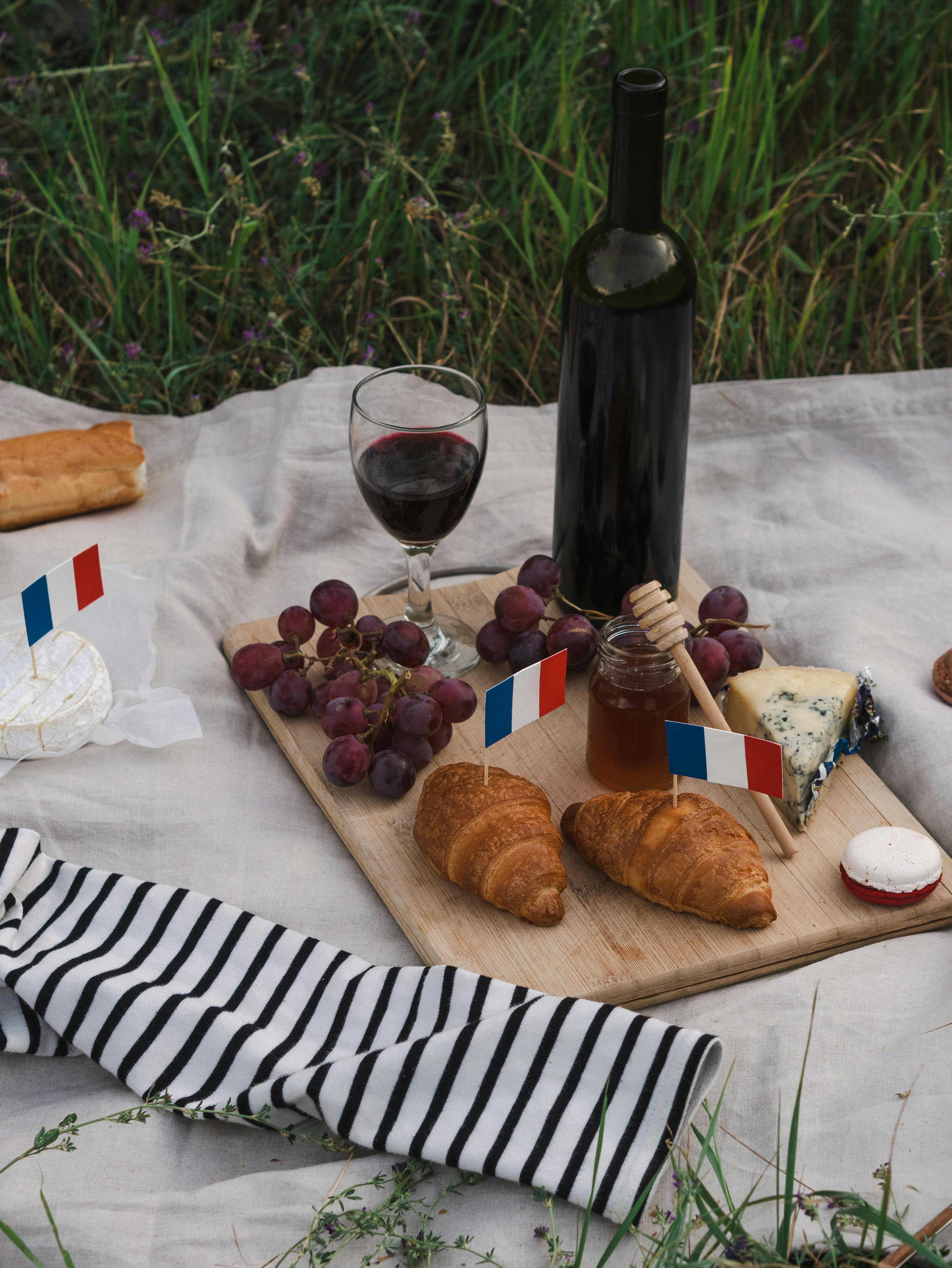 pastries and fruits with glass of wine on picnic blanket
