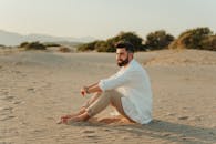 日落时分，一名男子赤脚坐在沙滩上的宁静场景