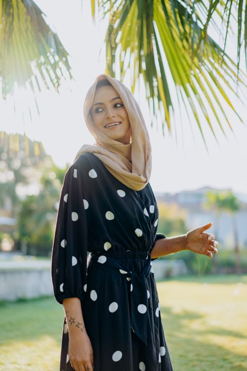 Free A young woman in a black polka dot dress and headscarf enjoys a sunny day outdoors. Stock Photo
