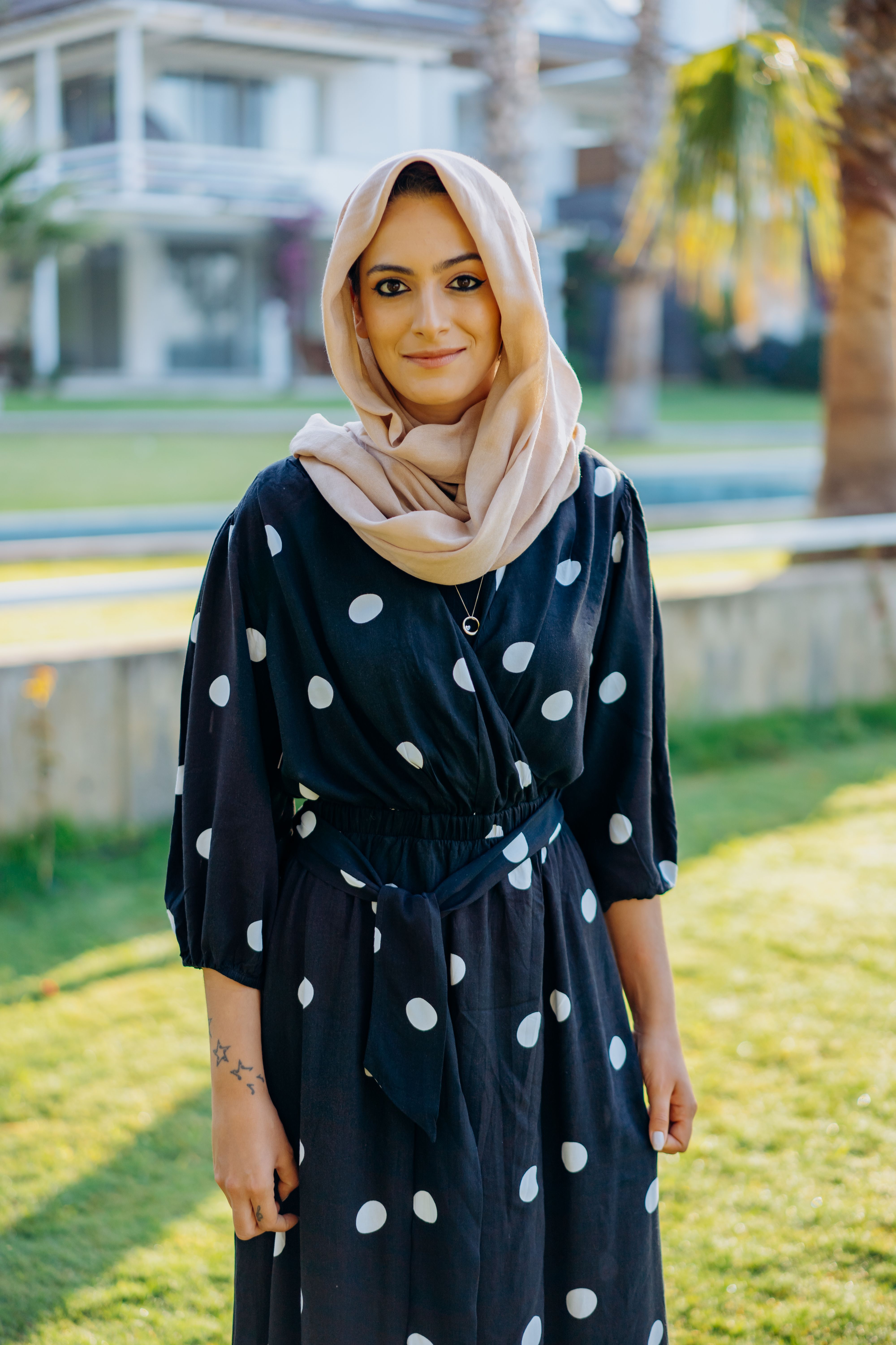 Stylish woman wearing a hijab and black polka dot dress in a sunny outdoor setting.