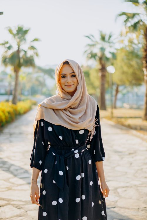 Free Charming woman in a polka dot dress and hijab smiling outdoors on a sunny day. Stock Photo