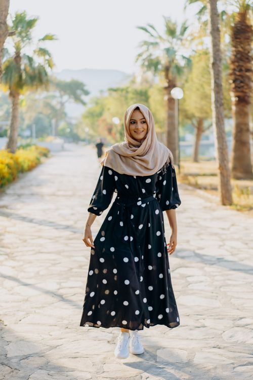 Free A woman in hijab wearing a polka dot dress is walking in a sunny park. Stock Photo