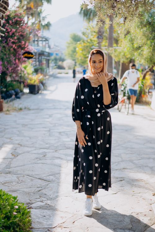 Free Stylish woman in hijab and polka dot dress strolling on a sunlit street, embodying modern fashion with traditional wear. Stock Photo
