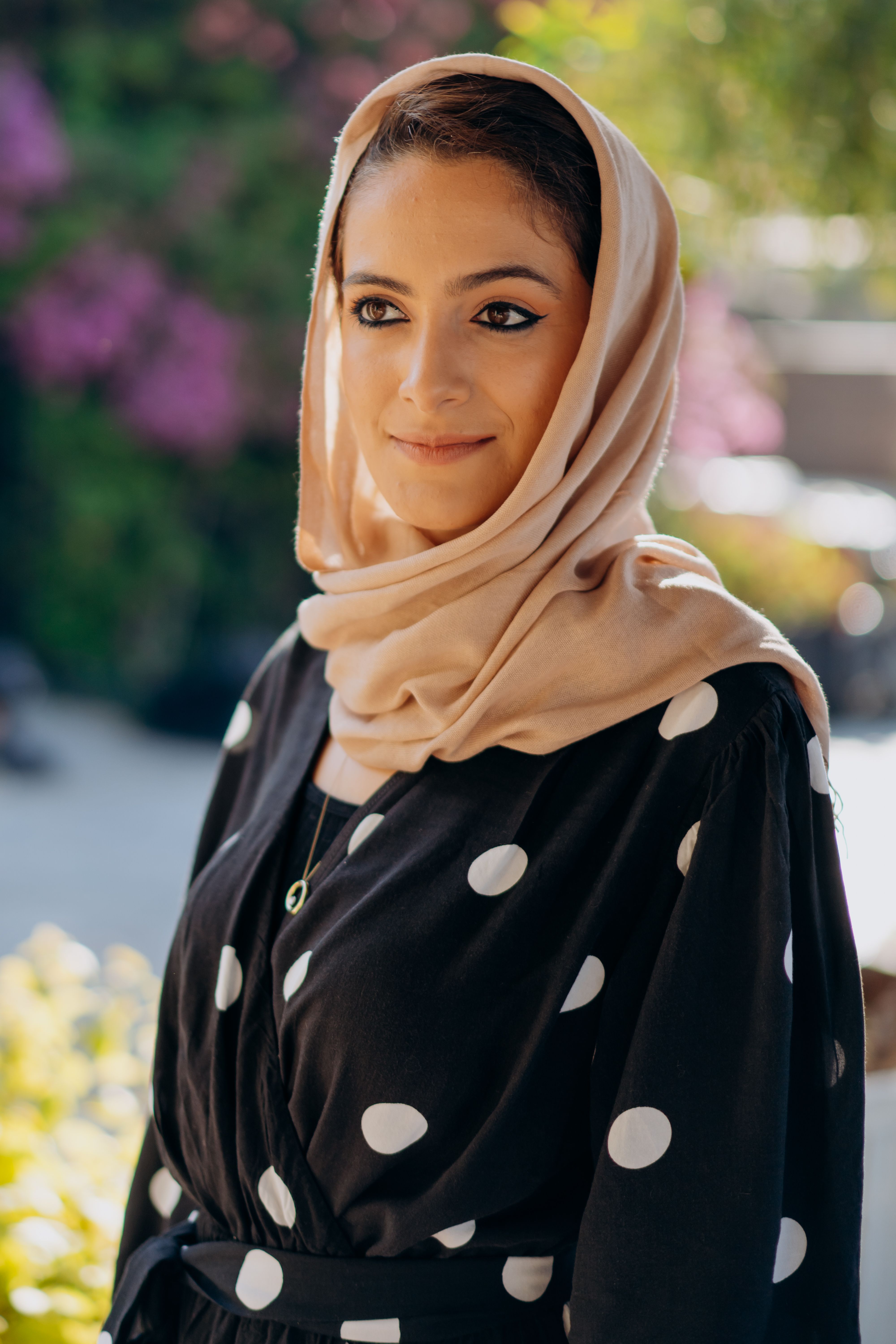 Elegant portrait of a woman wearing a hijab and polka dot dress outdoors.