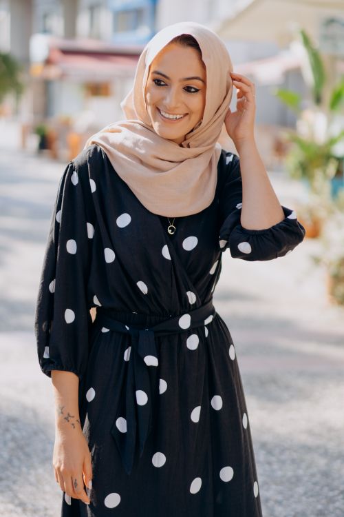 Free Charming woman outdoors in polka dot dress and hijab, smiling and posing joyfully. Stock Photo