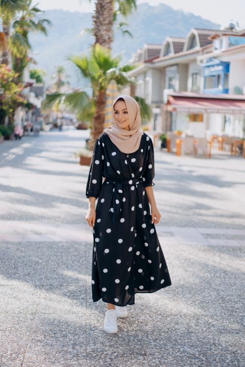 Free Smiling woman in polka dot dress and headscarf walking on a sunny street lined with palm trees. Stock Photo