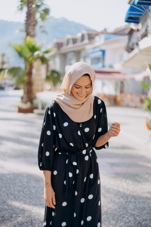 Free A joyful woman in a polka dot dress walks casually along a sunlit street lined with palm trees. Stock Photo