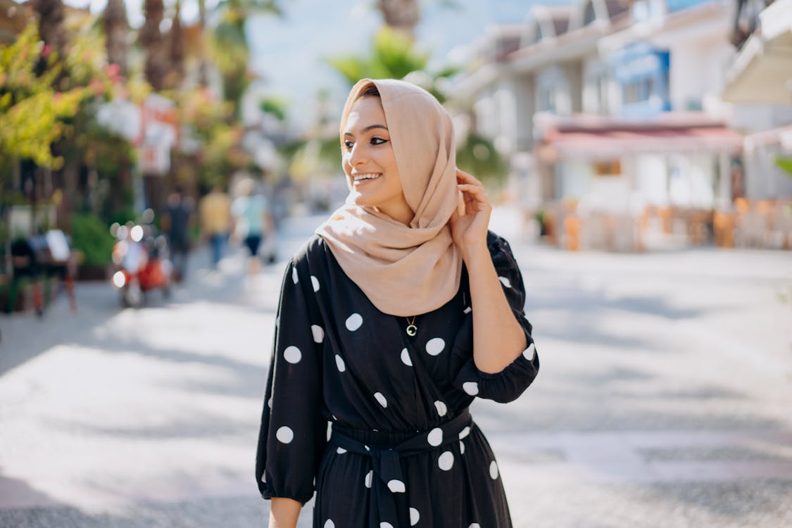 Бесплатные стоковые фото на тему головной платок, женщина, красивая,  ожерелье, пальцы, платье в горошек, рука, счастливый, улица, улыбка,  хиджаб, человек