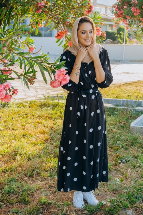 Free Smiling woman in a polka dot dress and hijab standing in a garden. Stock Photo