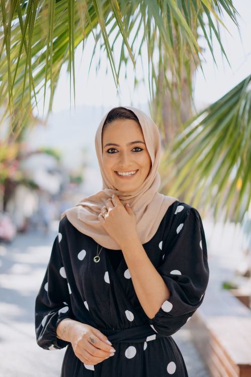 Free A smiling woman in a hijab stands outdoors under palm trees, embracing the sun. Stock Photo