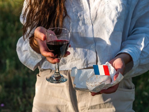 A Woman in White Long Sleeves Holding a Glass of Wine and a Cheese with Flag on Top