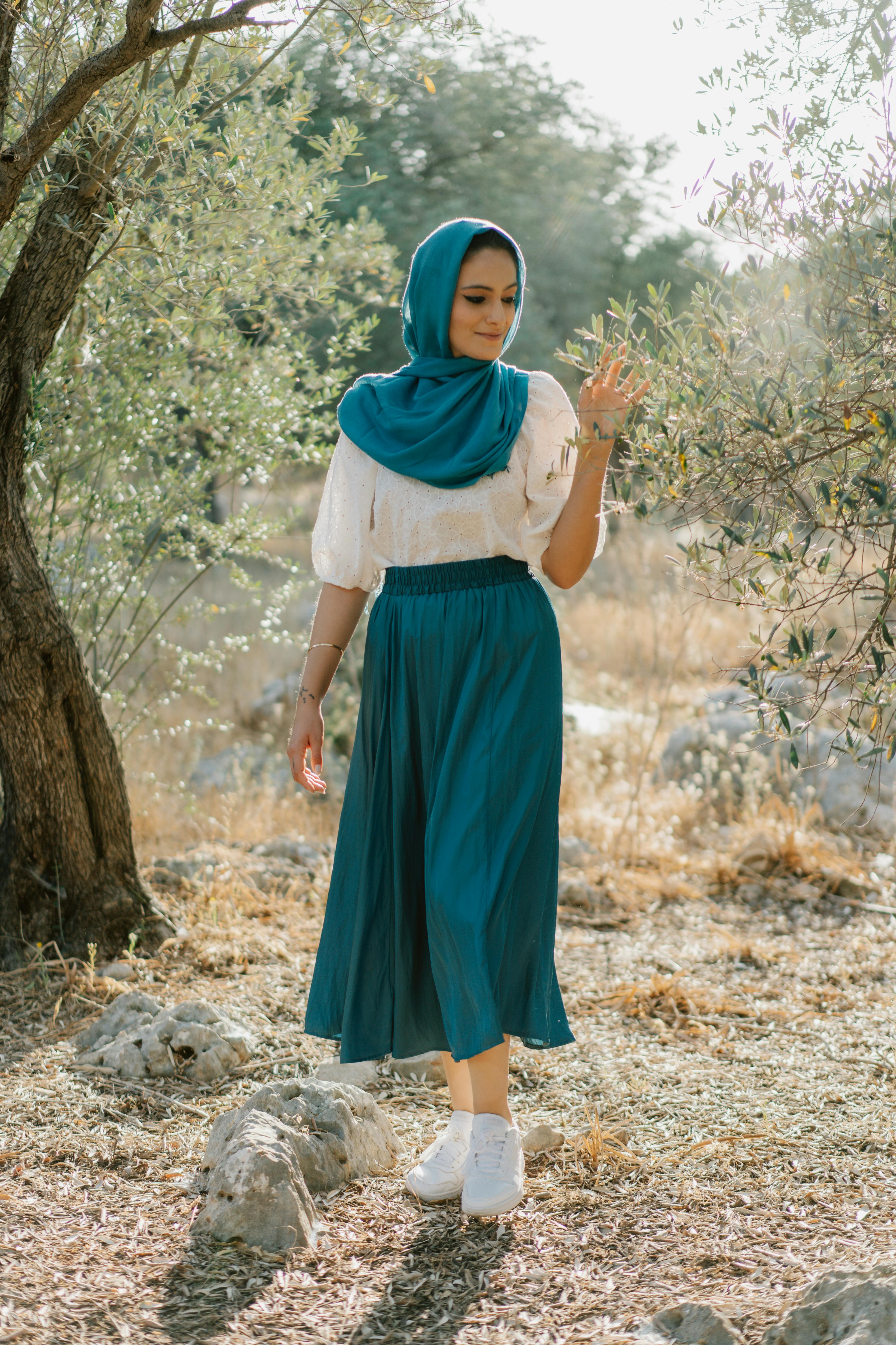 Woman in a blue hijab and skirt enjoying a peaceful moment outdoors.