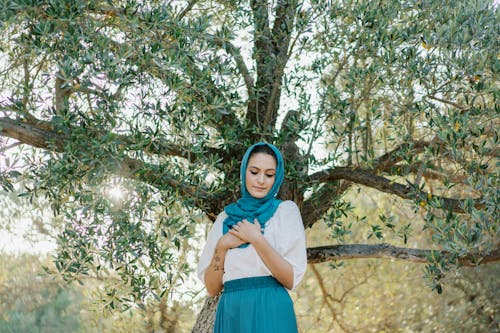 Free Woman Wearing Blue Headscarf Standing Beside a Tree Stock Photo