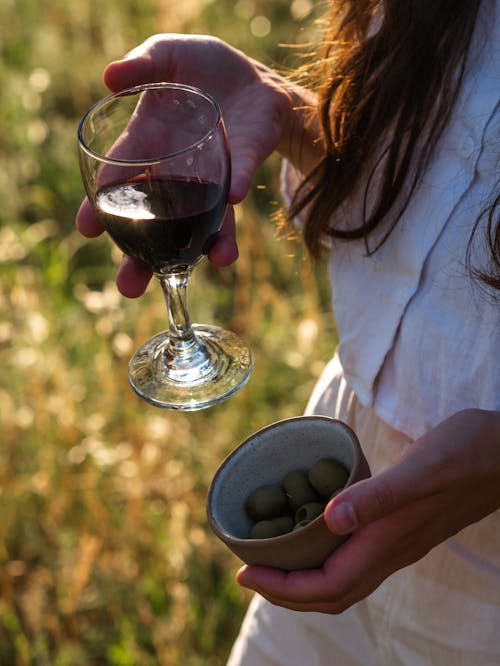 Free Woman Holding a Glass of Red Wine and Small Bowl of Olives Stock Photo