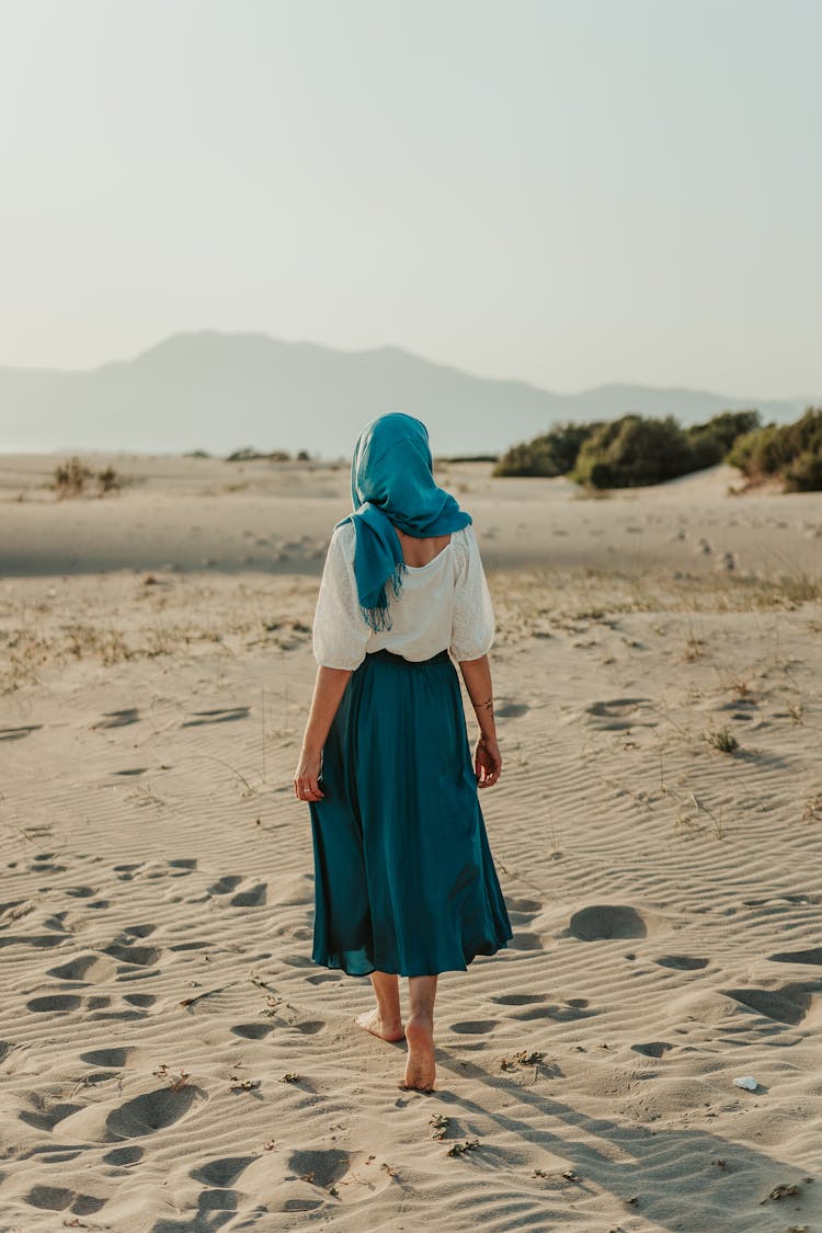 Woman In Blue Hijab Walking Barefoot On Sand On A Desert