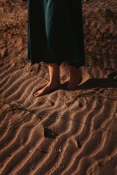 Barefoot feet stepping on sandy beach while wearing a flowing skirt, capturing a serene outdoor moment.