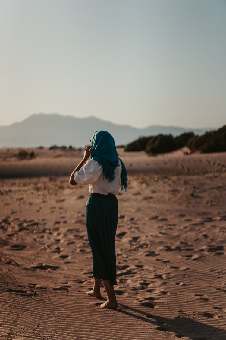 Woman In Blue Hijab Walking Barefoot On Sand On A Desert