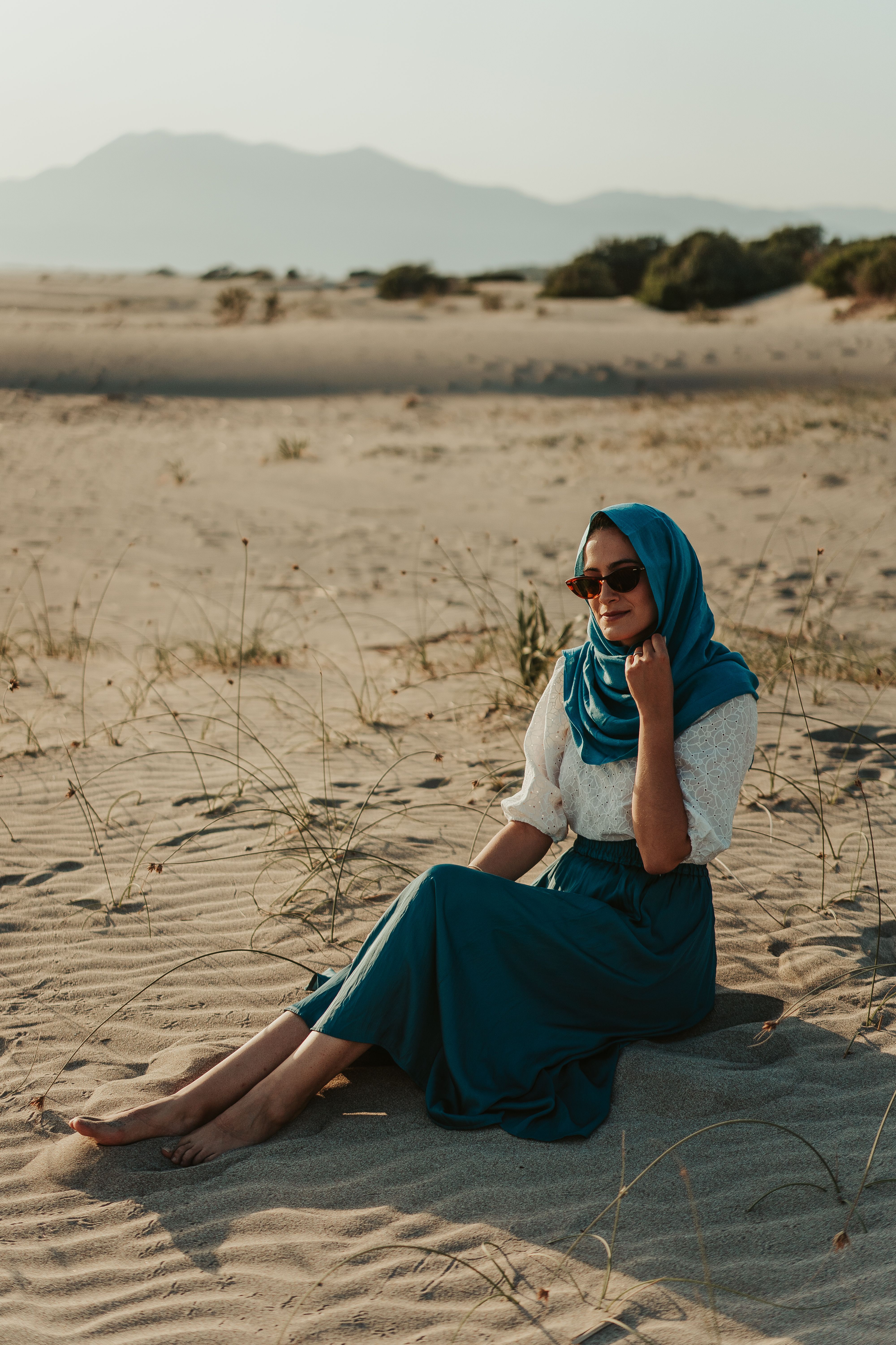 Woman in White Long Sleeve Shirt and Blue Skirt Sitting on Brown Sand ...