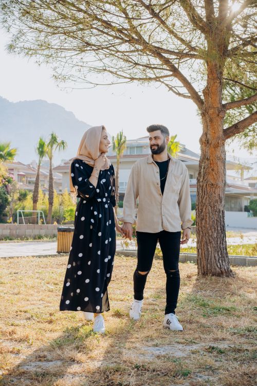 Free A young couple walking hand in hand on a sunny day, showcasing affection and style. Stock Photo